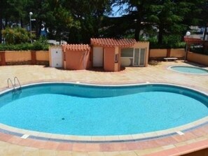 Ein Schwimmbecken mit gefliestem Sonnendeck, eine kleine Konstruktion mit Tür und eine Bank.