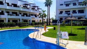 A swimming pool with a curved edge, surrounded by a well-maintained lawn and palm trees. - Bright apartment with AC - 6 guests (San Juan de los Terreros)