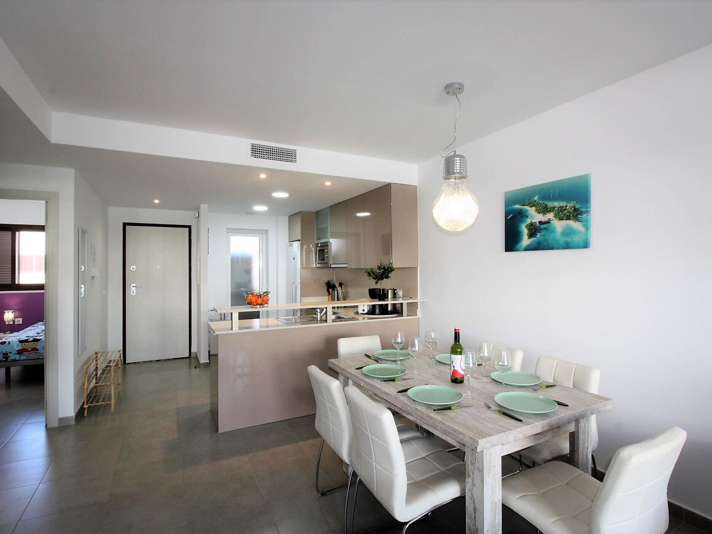 Cozinha moderna com ilha central, cadeiras de jantar brancas e mesa de madeira para seis pessoas.