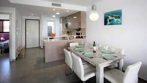 A modern kitchen with a central island, white dining chairs, and a wooden table set for six. - Bright apartment with AC - 6 guests (San Juan de los Terreros)