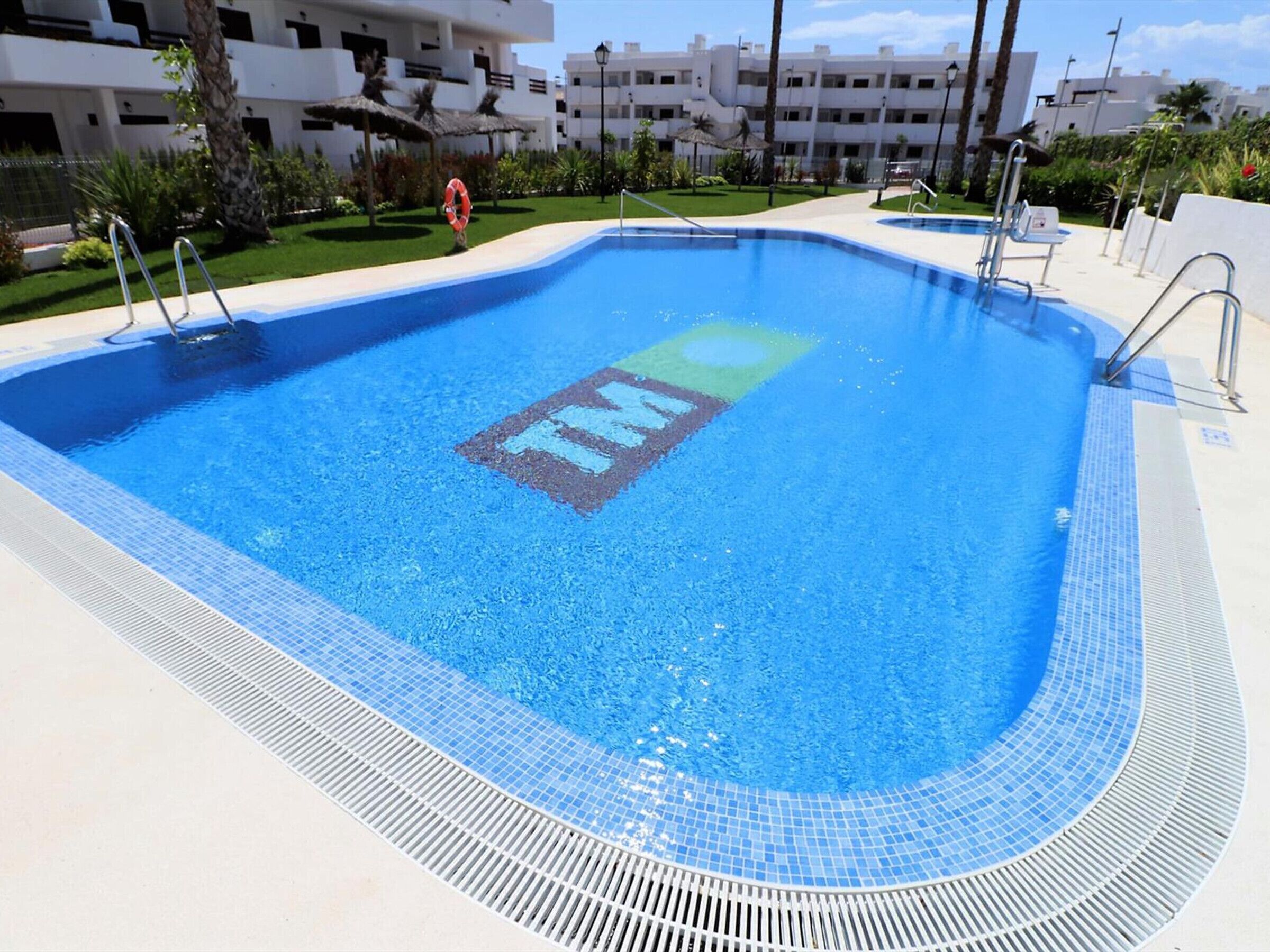 A swimming pool with a lifebuoy, poolside chairs, and a palm tree.