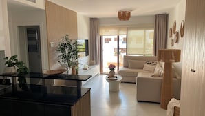 Ein modernes Wohnzimmer mit einer Couch, einem Couchtisch und einem Fernseher. Es gibt eine Küchenzeile mit schwarzer Arbeitsplatte und Schränken.