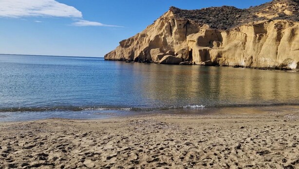Ein Strand mit einer felsigen Klippe und ruhigem Meer.