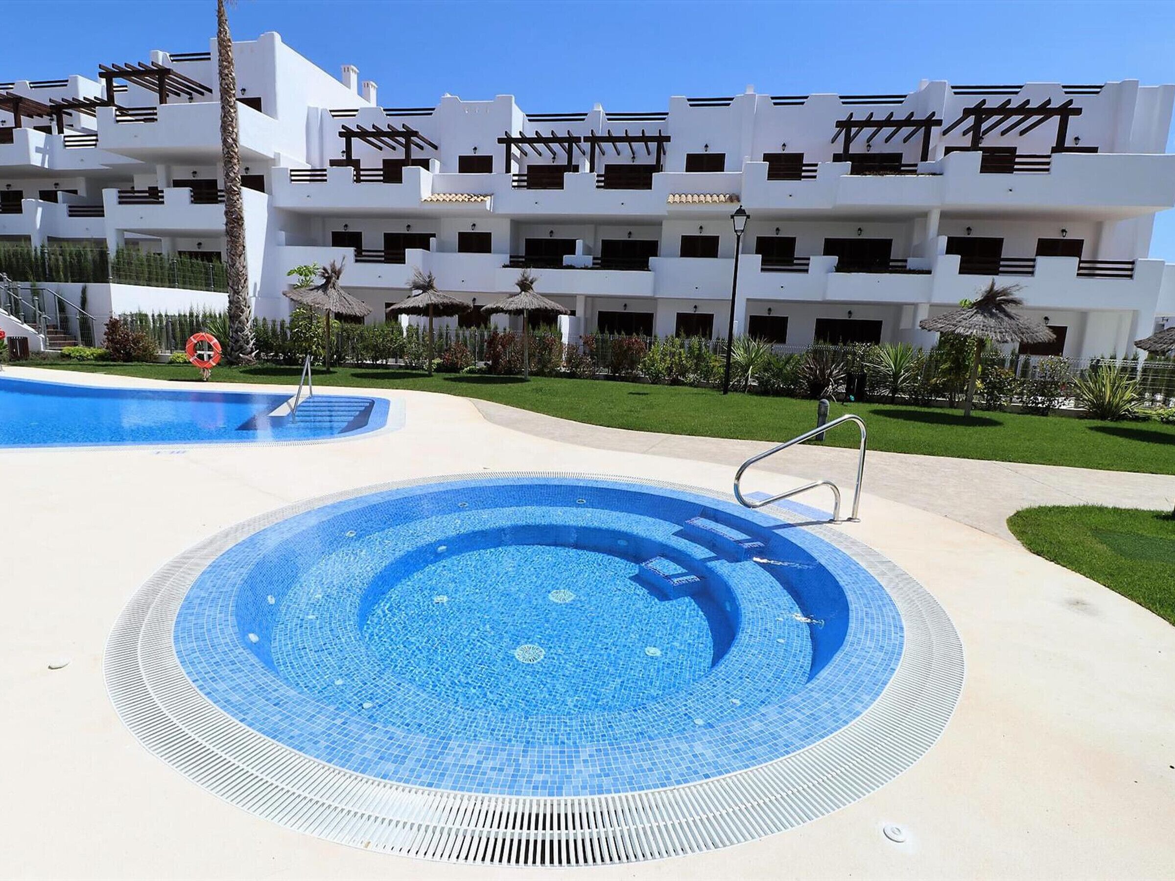 Un área de piscina con dos piscinas circulares, una palmera y un edificio con balcones.