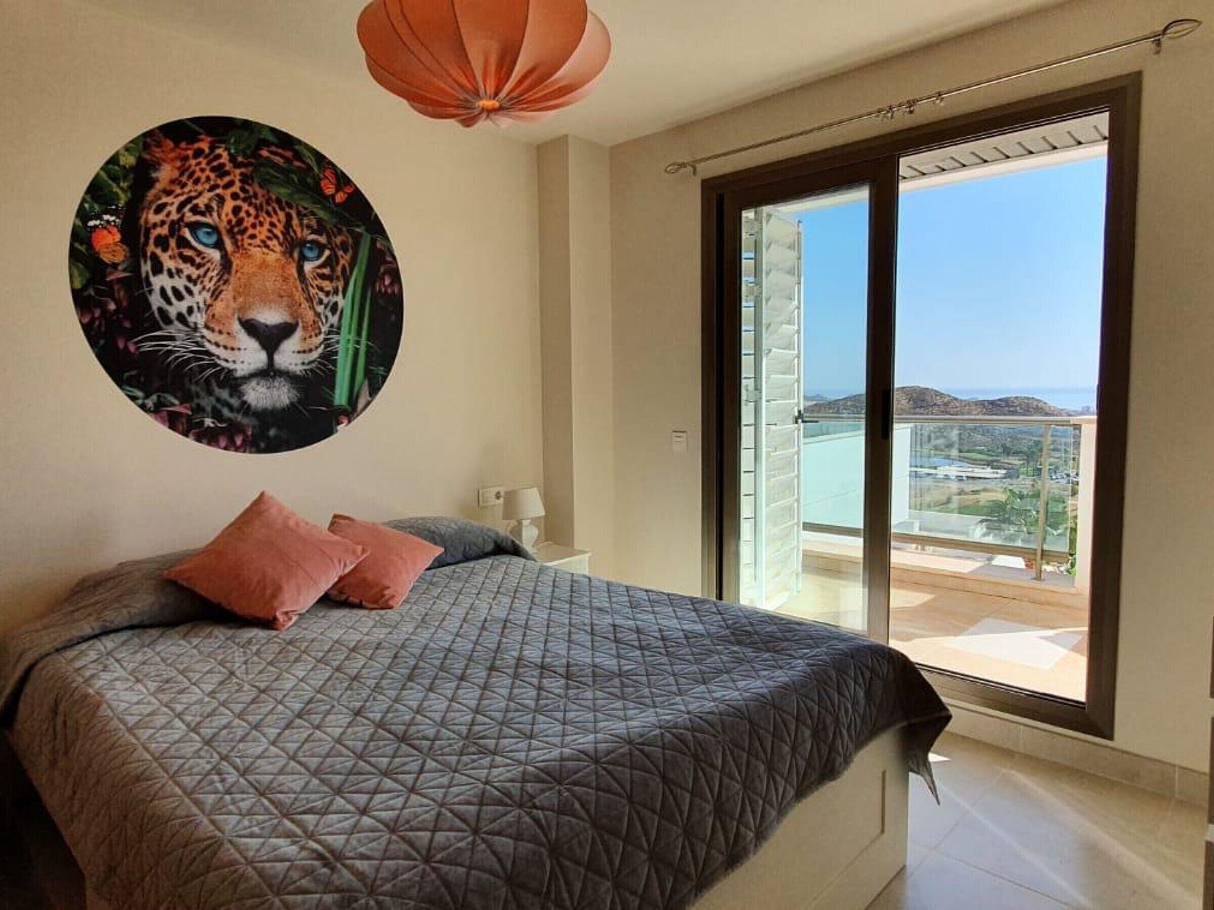 Een slaapkamer met een groot bed, een wanddecoratie met luipaardprint, een balkon met uitzicht en een hanglamp.