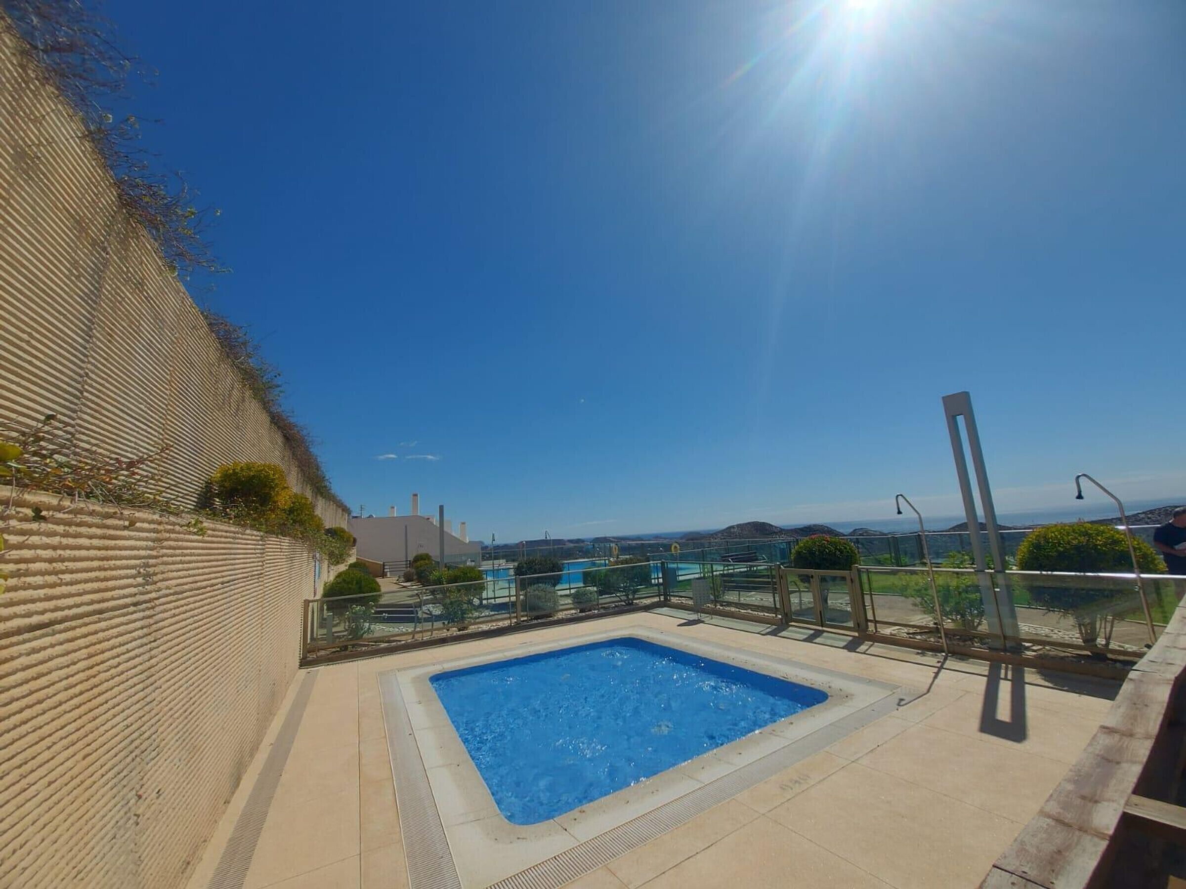 Une piscine sur le toit, avec une eau d’un bleu limpide, entourée d’une rambarde en verre et offrant une vue sur les collines lointaines.