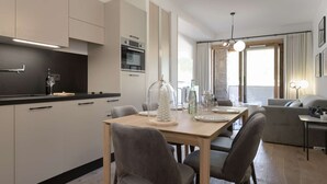 Eine moderne Küche mit integrierten Geräten, ein Essbereich mit Tisch und Stühlen sowie ein Wohnbereich mit einer Couch und einer Lampe.
