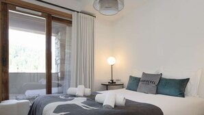 Ein Schlafzimmer mit Bett, Kissen, einem Nachttisch, einer Lampe und Blick durch ein Fenster.