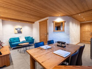 A dining area with a wooden table, chairs, a blue sofa, and a small side table with a decorative item. - Cozy apartment with Wi-Fi - 2 guests (Les Gets)