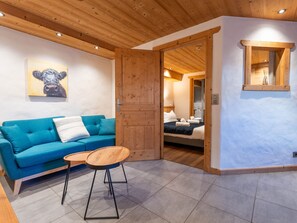 A room with a blue sofa, a wooden table, a wooden door leading to a bedroom, and a painting on the wall. - Cozy apartment with Wi-Fi - 2 guests (Les Gets)