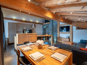 A modern kitchen with wooden beams, a dining area with a wooden table set for four, and a stone wall. - Cozy apartment, Wi-Fi - 6 guests (Les Gets)