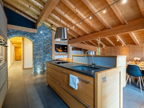 A modern kitchen with wooden beams, a stone wall, and a dining area with a table and chairs. - Cozy apartment, Wi-Fi - 6 guests (Les Gets)