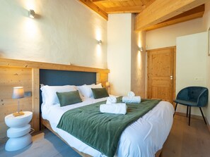A bedroom with a bed, bedside lamps, a chair, and a wooden door. - Spacious apartment with Wi-Fi - 6 guests (Les Gets)
