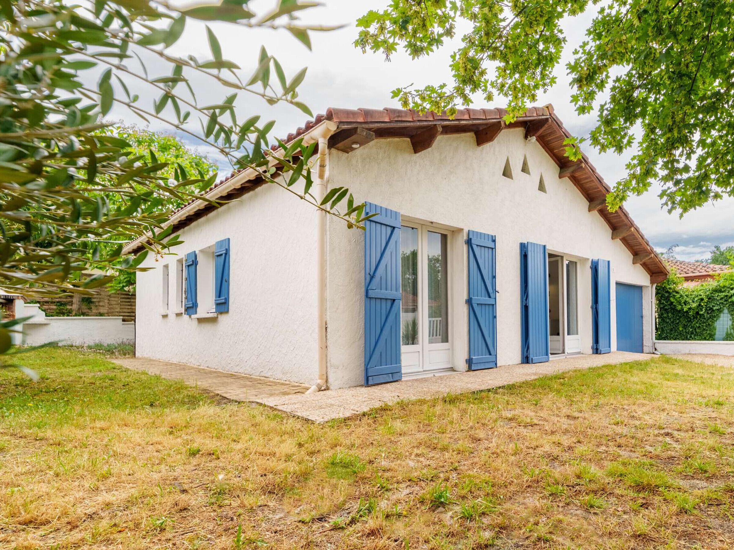 Ein eingeschossiges Haus mit weißer Fassade, blauen Fensterläden und einem Ziegeldach.