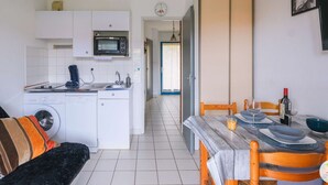 Una cocina compacta con microondas, fregadero y lavadora, una zona de comedor con mesa y sillas, y un espacio de sala con sofá.
