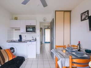 A compact kitchen with a microwave, sink, and washing machine, a dining area with a table and chairs, and a living space with a sofa. - Cozy 1-Star Apartment with Terrace, Parking, Near Beach - Sleeps 4 (Biscarrosse)