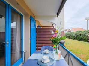 A balcony with a table set for two, a potted plant, and a view of a residential area. - Cozy 1-Star Apartment with Terrace, Parking, Near Beach - Sleeps 4 (Biscarrosse)