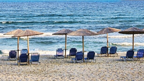Una playa con filas de sillas de descanso y sombrillas de paja.
