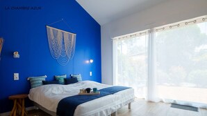 A bedroom with a bed, a blue wall, a hanging macrame wall art, a window with curtains, and a wooden floor. - 5-star villa, heated pool, 4 rooms with private baths and BBQ - Up to 12 guests (Parentis-en-Born)