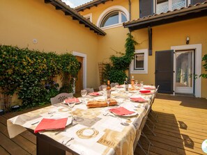 An outdoor dining area with a table set for four, surrounded by greenery and a yellow building. - 5-star villa, heated pool, 4 rooms with private baths and BBQ - Up to 12 guests (Parentis-en-Born)
