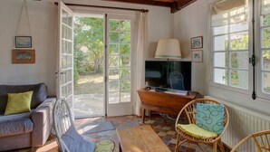 A room with a wooden ceiling, a sofa, a chair, a television, and a window with a view of greenery. - Charming 2-bedroom house with garden near the lake, perfect for holidays (Sanguinet)