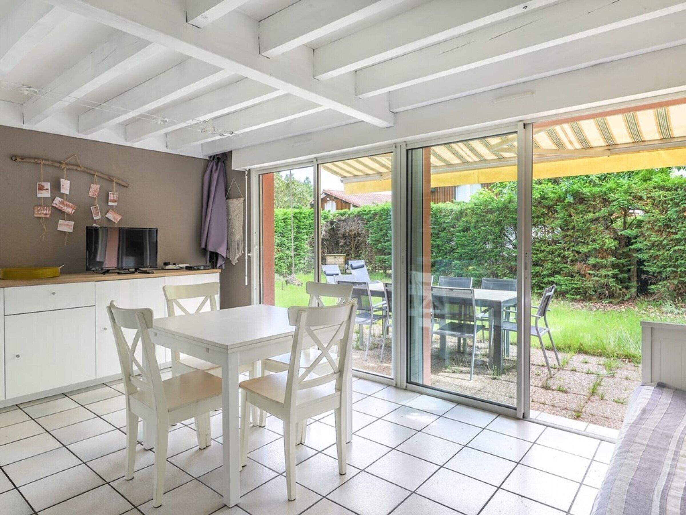 A modern kitchen with white cabinets, a dining area with white chairs, and a sliding glass door leading to a patio with outdoor seating.