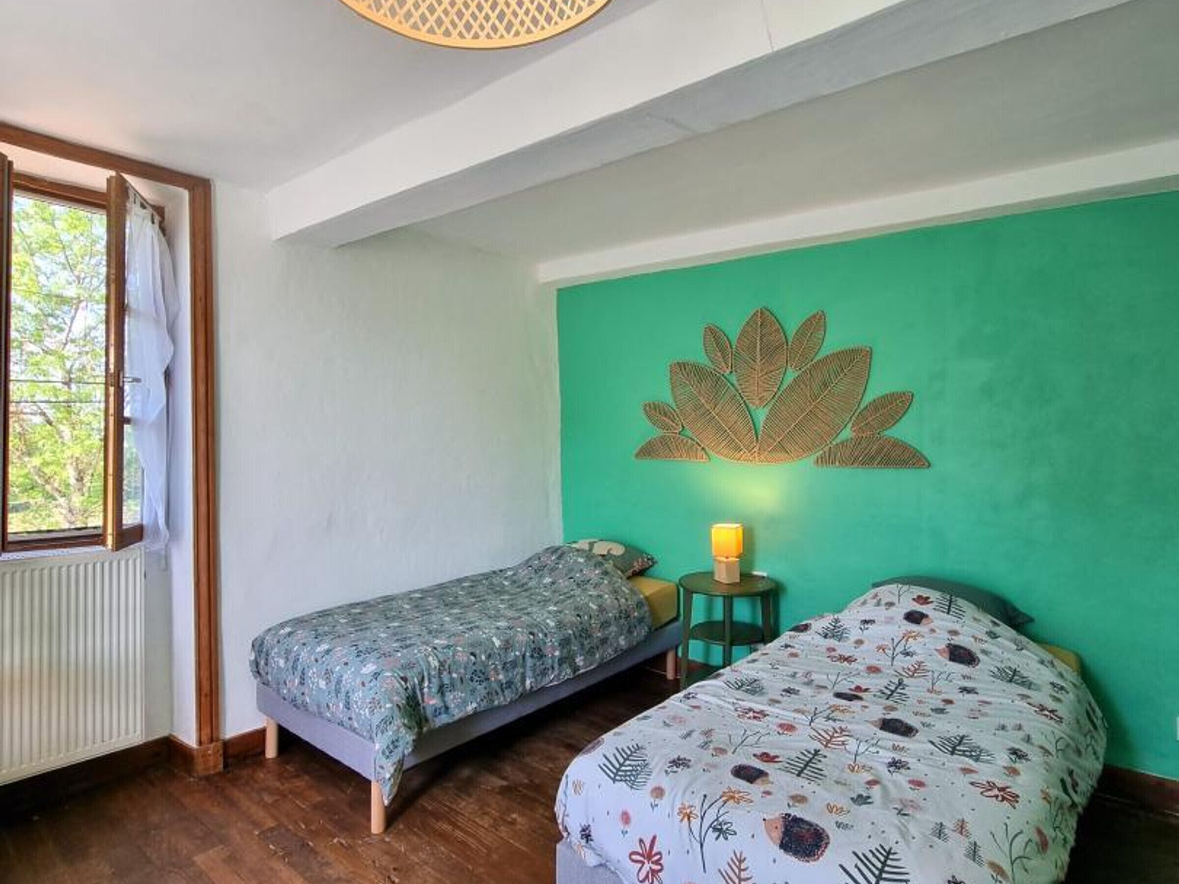 Une chambre avec deux lits, une fenêtre avec des rideaux, une lampe fixée au mur et un mur de couleur verte.