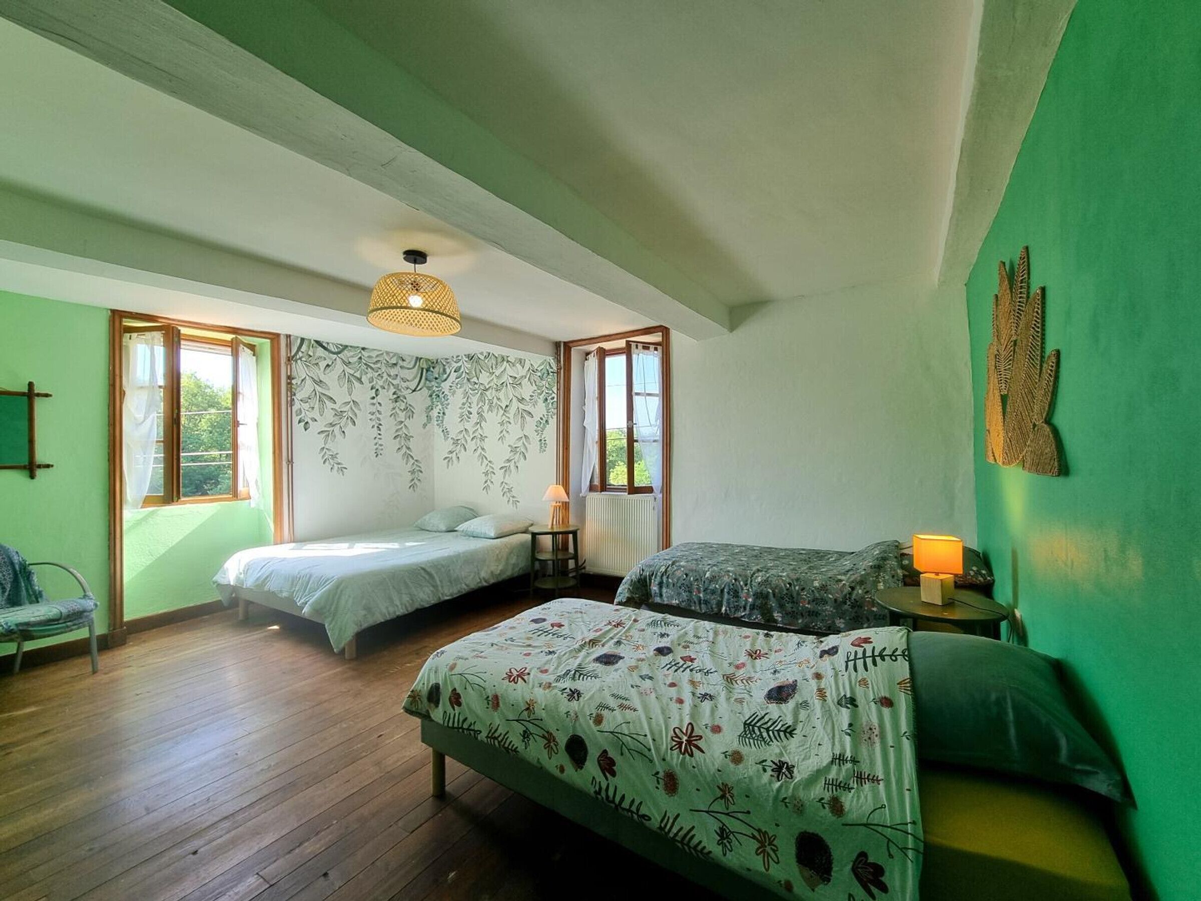 A bedroom with two beds, a hanging light fixture, a window, and a green wall.