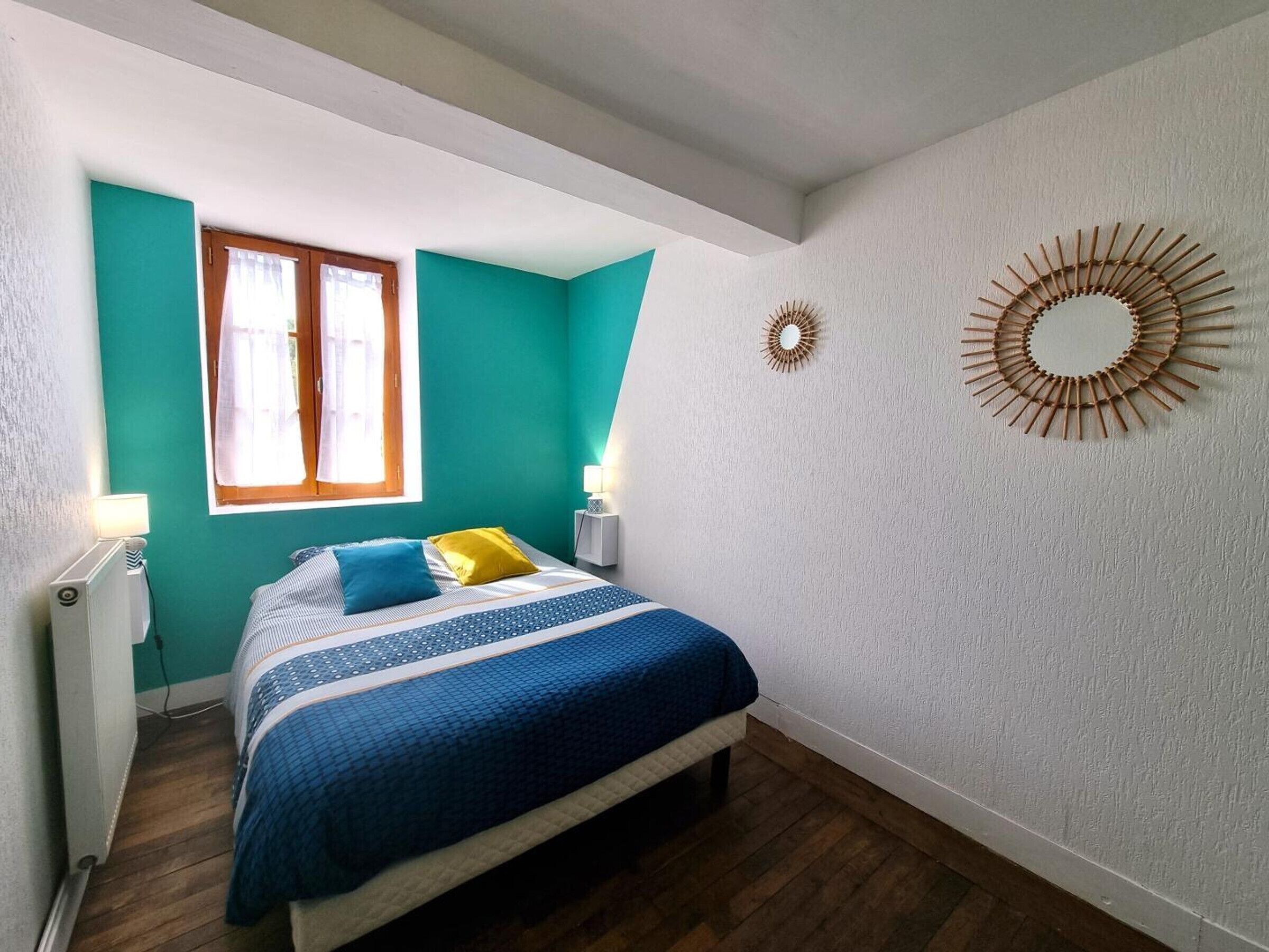 A bedroom with a bed, a window, a wall-mounted mirror, and a radiator.
