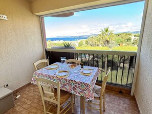 Uma varanda com uma mesa posta para dois, cadeiras e vista para o mar e vegetação.
