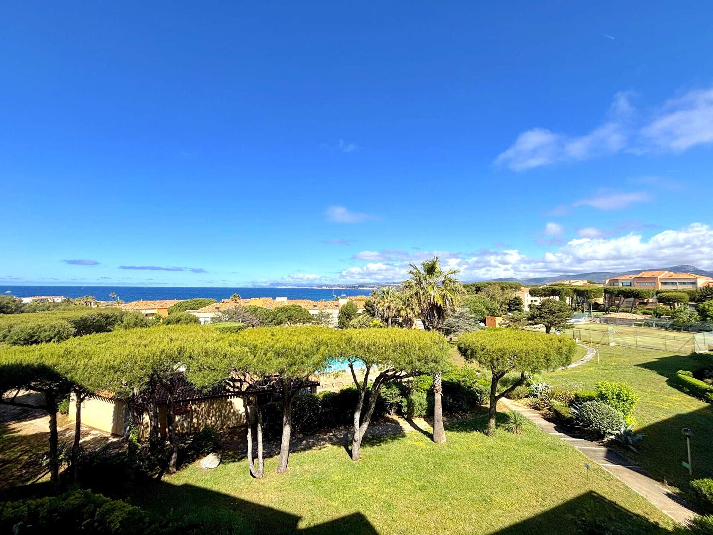 A residential area with a view of the sea, a well-maintained garden, and a clear sky.