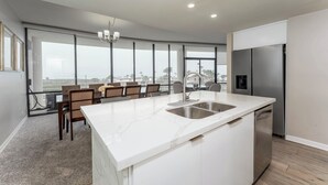 Une cuisine moderne dotée d’un grand îlot central, d’appareils électroménagers en acier inoxydable et offrant une vue dégagée grâce à de grandes fenêtres.