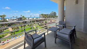 Un balcon avec deux chaises et une table, donnant sur un espace aménagé avec des palmiers et un court de tennis.