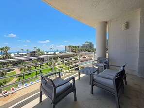 Ein Balkon mit zwei Stühlen und einem Tisch, der auf eine angelegte Grünfläche mit Palmen und einem Tennisplatz blickt.