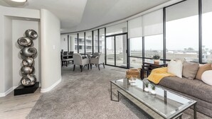 Un salon moderne doté d’un plafond incurvé, d’une table basse en verre, d’un canapé gris et d’un coin repas avec une table et des chaises.