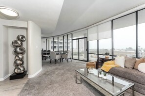 Ein modernes Wohnzimmer mit gewölbter Decke, einem Glastisch, einem grauen Sofa und einem Essbereich mit Tisch und Stühlen.