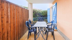 A covered patio with a table and chairs, a wooden fence, and a blue door. - Biscarrosse Beach Apt Terrace 4 pax with Parking (Biscarrosse)