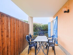 Eine überdachte Terrasse mit Tisch und Stühlen, ein Holzzaun und eine blaue Tür.