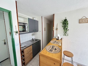 A compact kitchen with a built-in oven, a sink, and a wooden bar counter with stools. - Bright apartment, pool view, parking - 4 guests (Argelès-sur-Mer)