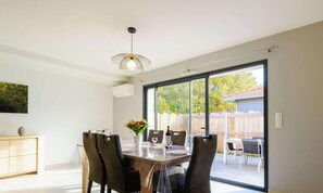 A dining area with a table set for four, a pendant light, and a sliding glass door leading to an outdoor patio. - Charming Villa in Biscarrosse with Garden, 3 Bedrooms, and Terrace - Perfect for 6 Guests (Biscarrosse)