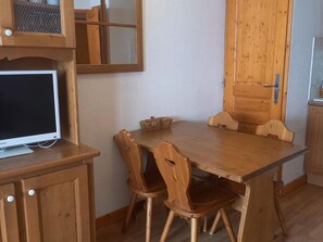 A wooden dining table with two chairs, a television on a cabinet, and a wooden door with a handle. - Cozy apartment, south terrace - 4 guests (Valloire)