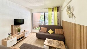 Un salon moderne avec un canapé, un téléviseur, une petite table en bois et une fenêtre avec des rideaux.