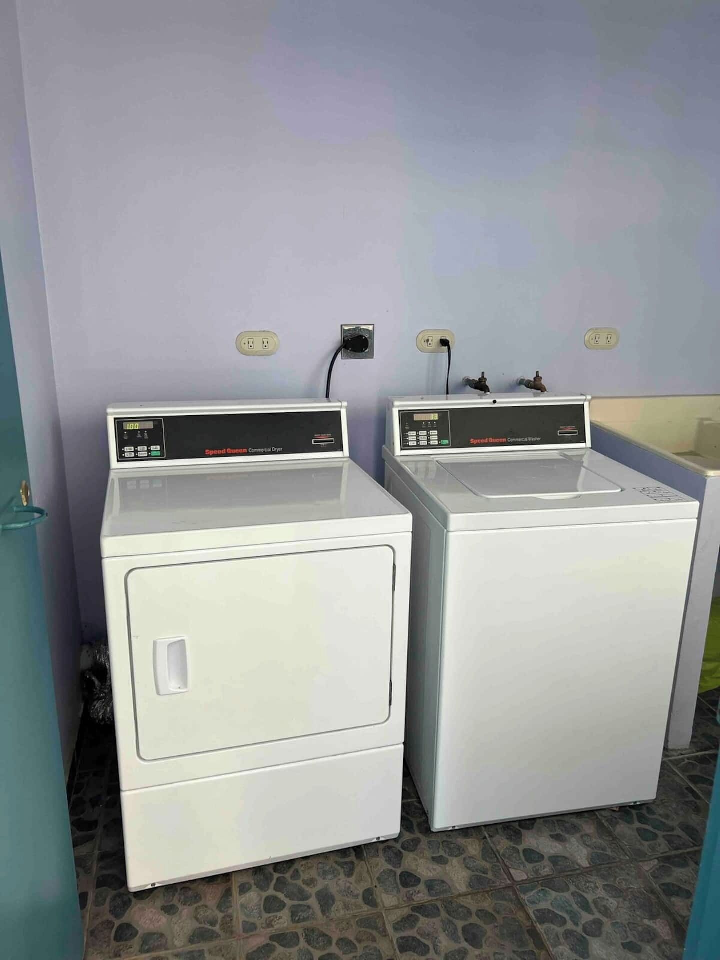 Two white commercial dryers side by side with control panels, connected to wall sockets.