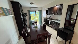 A compact kitchen with dark cabinets, a dining table with chairs, and a small window with curtains. - This beautiful 2-bedroom, 2-bath condo is a true gem (Playas Del Coco)