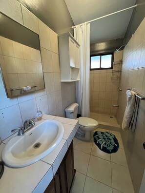 A bathroom with a sink, toilet, shower, and a small window. - This beautiful 2-bedroom, 2-bath condo is a true gem (Playas Del Coco)
