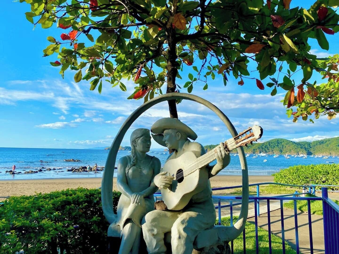 A sculpture of a man and woman under a tree by the beach.