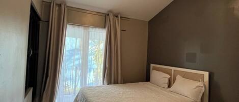 A bedroom with a bed, an air conditioning unit, a ceiling fan, and a window with curtains.