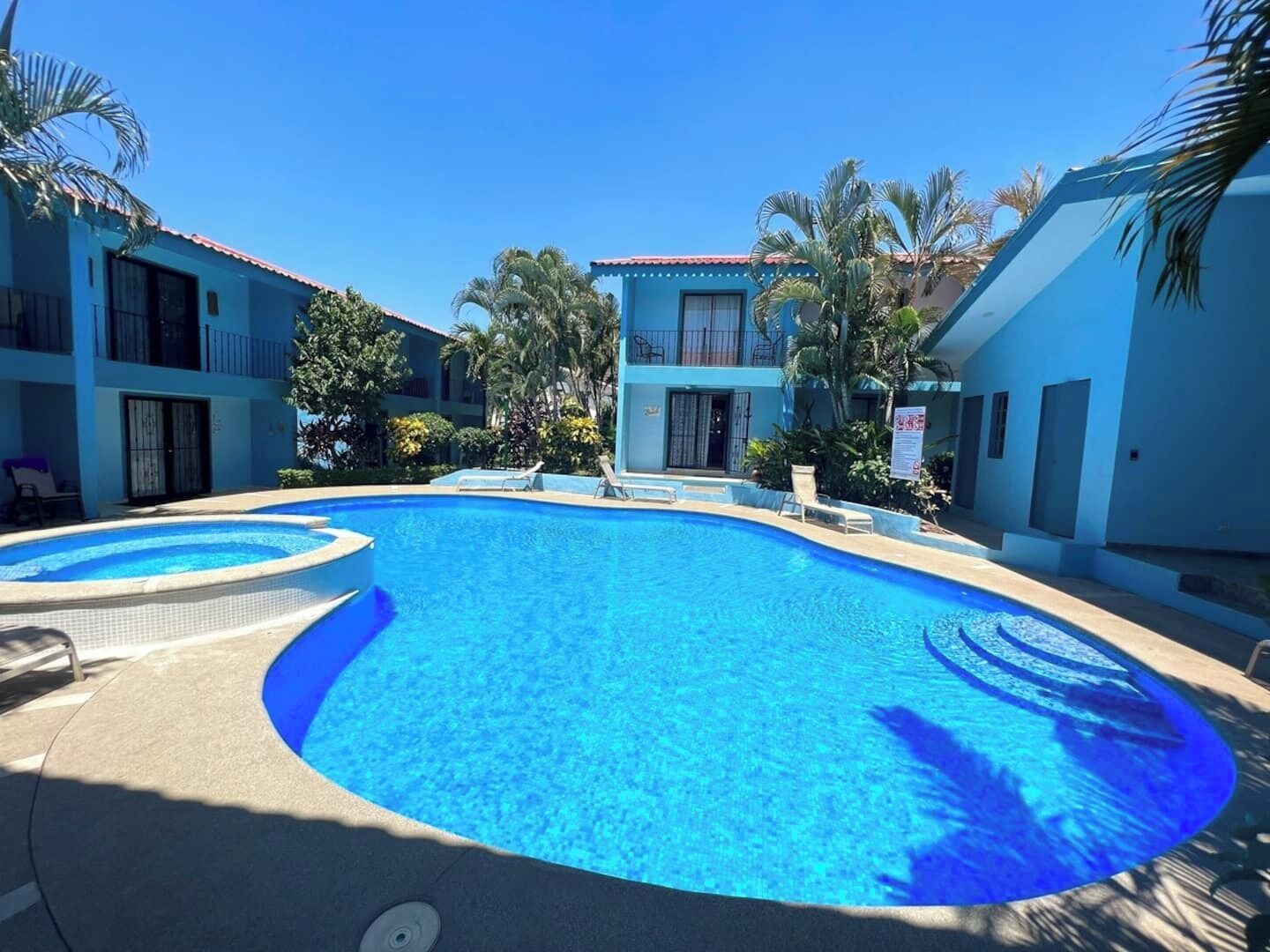 A swimming pool surrounded by buildings with balconies and palm trees.