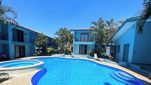 A swimming pool surrounded by buildings with balconies and palm trees. - This beautiful 2-bedroom, 2-bath condo is a true gem (Playas Del Coco)