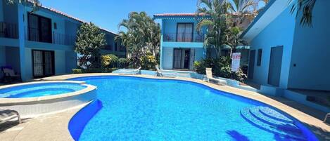 A swimming pool surrounded by buildings with balconies and palm trees.